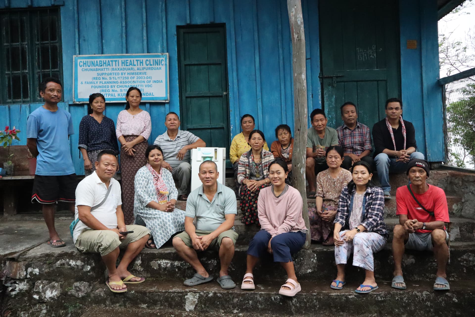 Community members and health volunteers gathered on the steps of the Chunabhatti Health Clinic in Alipurduar, supported by HIMserve